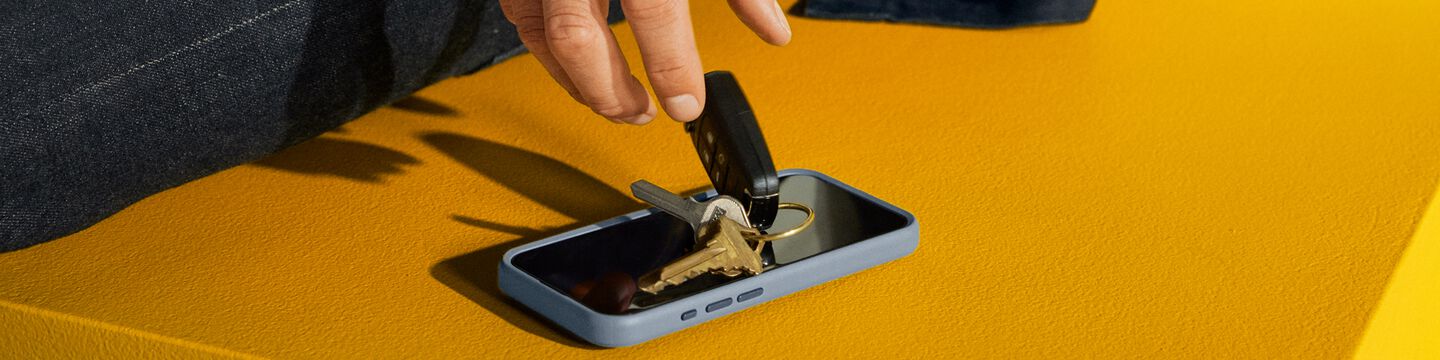 Man dropping keys on an iPhone with OtterBox glass screen protector on a yellow background