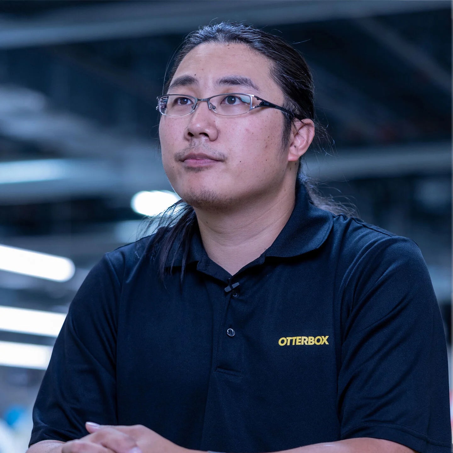 Man wearing glasses and an OtterBox shirt in a blurred indoor setting