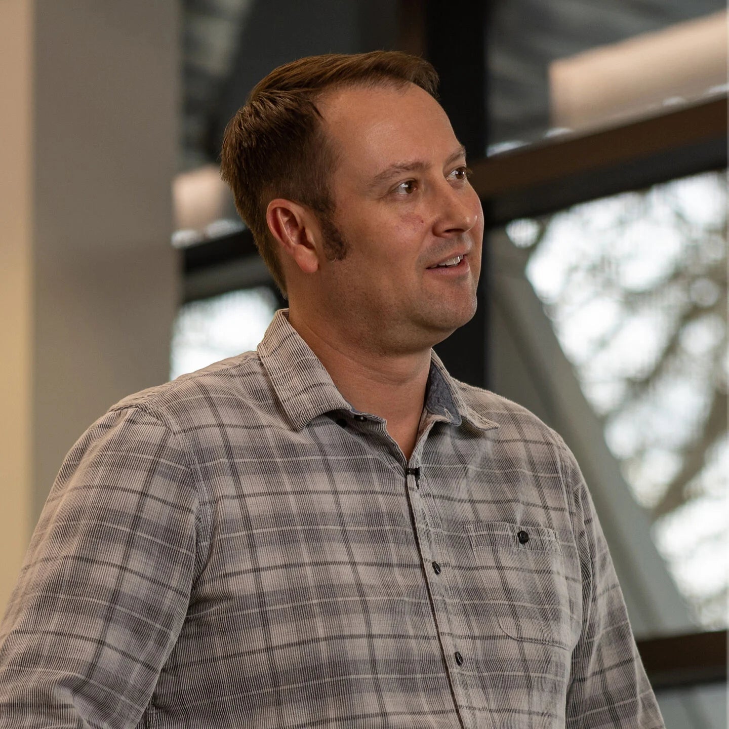 Man wearing a plaid shirt standing outdoors with blurred background