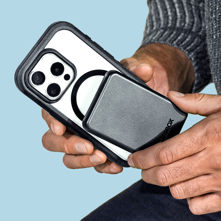Person holding a phone with a black case against a light blue background