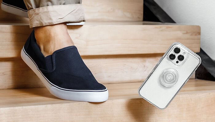 Person wearing navy slip-on shoes sitting on wooden steps with a smartphone next to them.