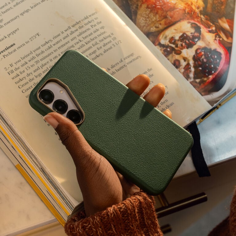 Green phone case held by a hand with a book and food in the background