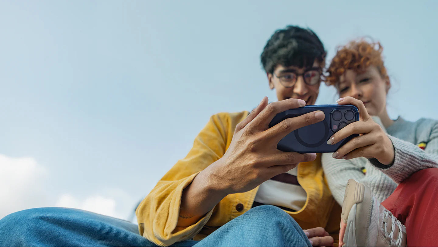 Two people sitting together, looking at a phone with a clear blue sky in the background.