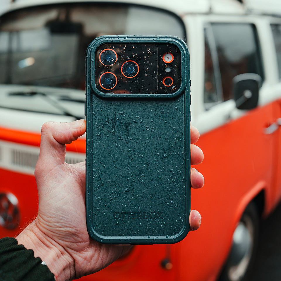 Person holding a black phone case in the rain with a red and white van in the background