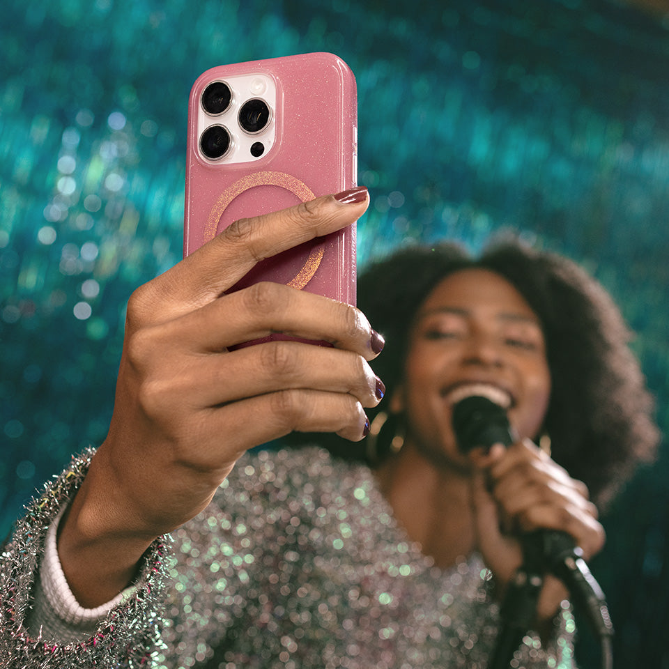 Person holding a pink phone case with a blurred background of a person singing into a microphone.