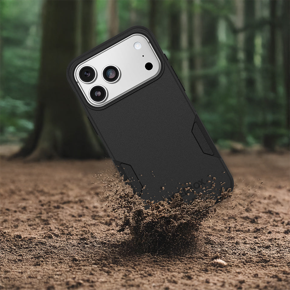 Black phone case being dropped onto dirt with a blurred forest background