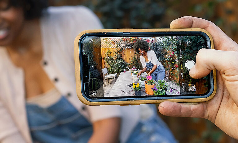 phone with yellow case snapping picture of woman gardening